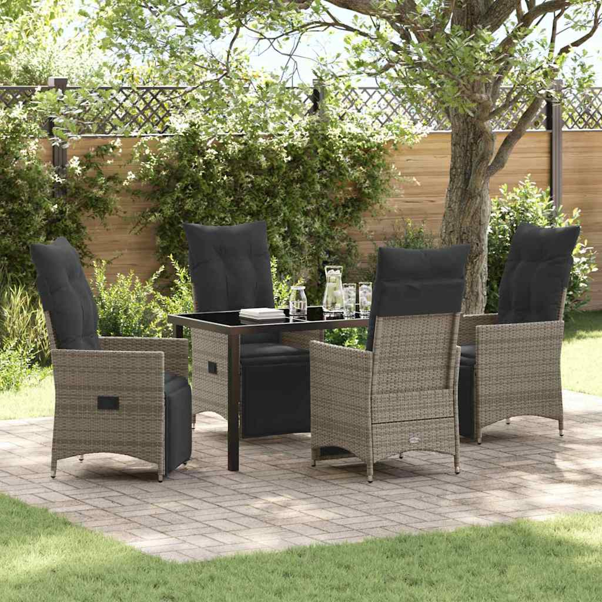 Terrassenset: Tisch mit schwarzer Platte, vier Korbstühle mit schwarzen Kissen. Grünes Gras und Bäume im Hintergrund.