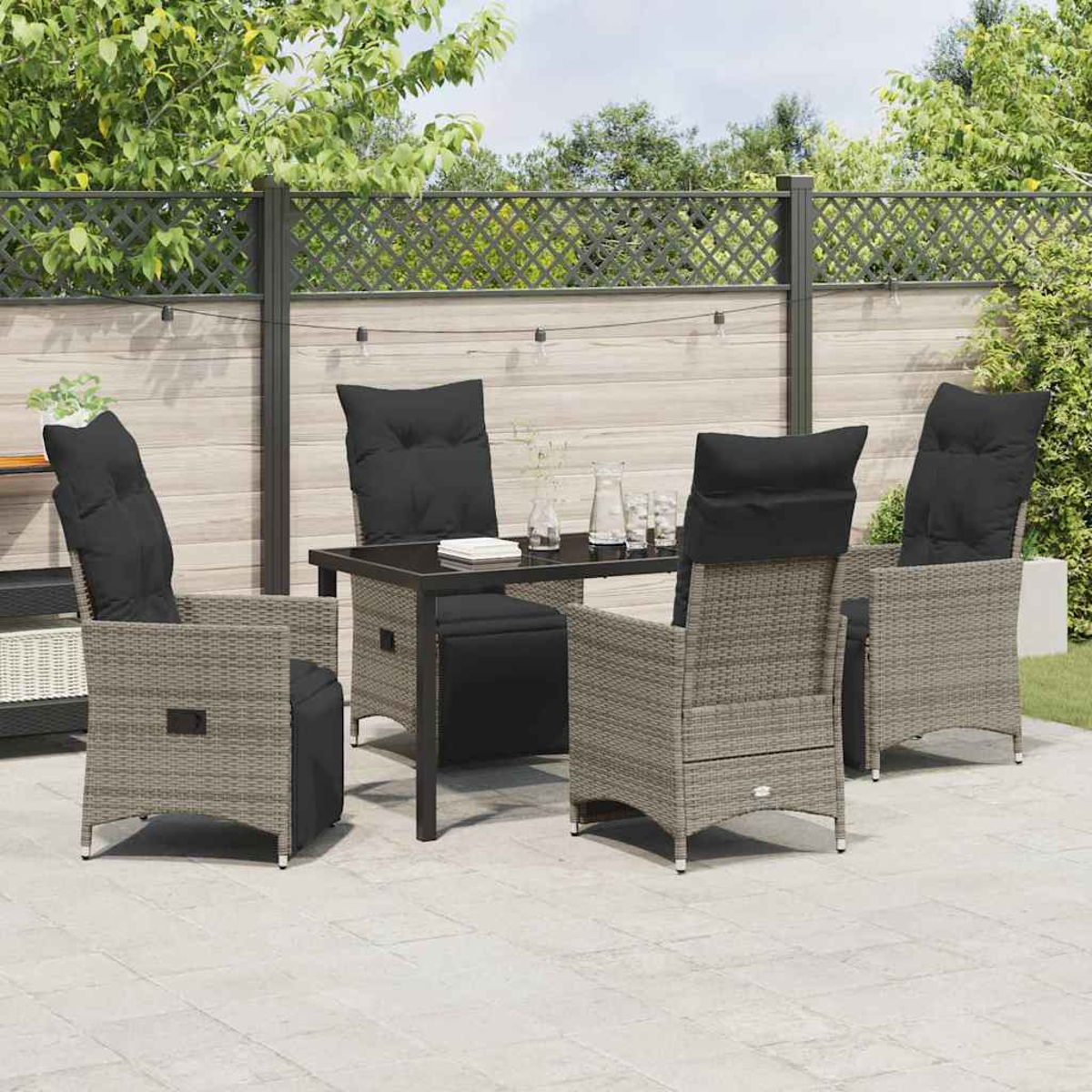 Terrassenset im Freien mit grauen Korbstühlen, schwarzen Kissen und einem schwarzen Tisch auf einer grauen Steinveranda mit Holzzaun.