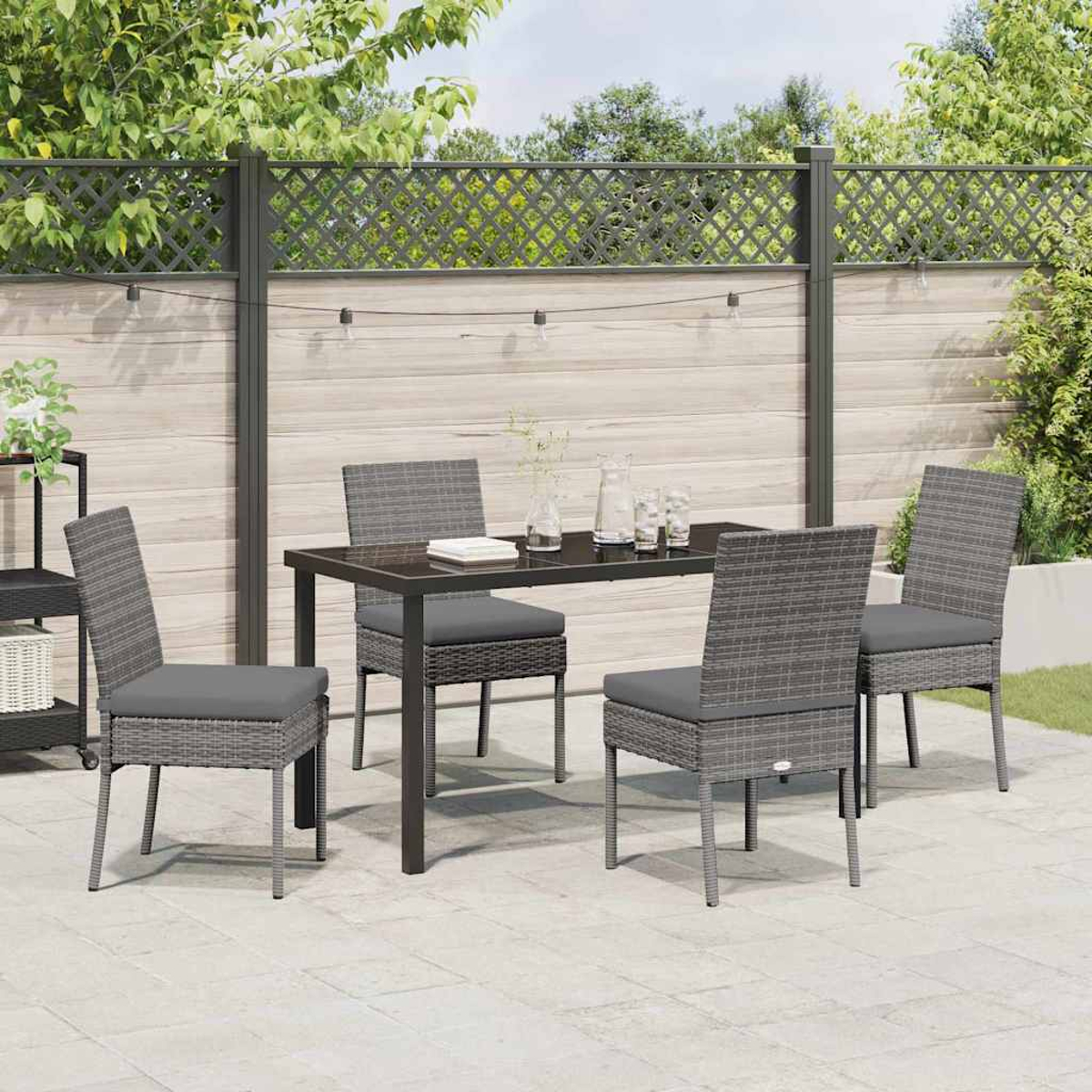 Essgruppe im Freien mit grauen Korbstühlen und einem schwarzen Tisch. Die Szene spielt sich auf einer Terrasse mit Zaun ab.
