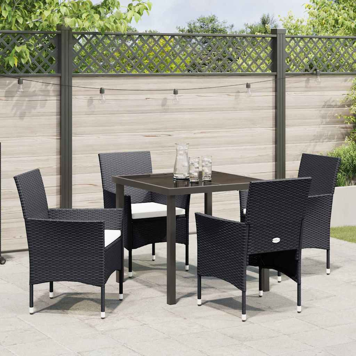 Un set da patio con quattro sedie in vimini nero e un tavolo quadrato. Il tavolo ha una brocca e bicchieri. Una recinzione sullo sfondo.
