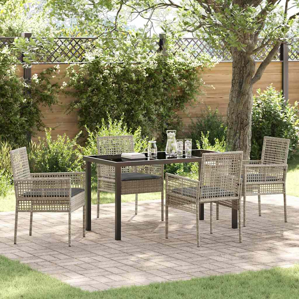 Set da patio all'aperto con tavolo, sedie e bevande. Lo sfondo presenta alberi, vegetazione e una staccionata in legno.