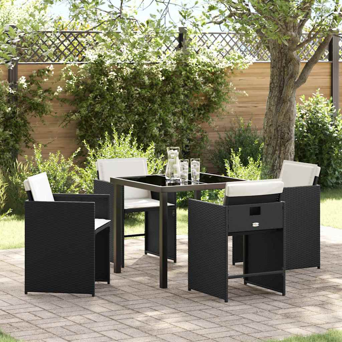 Set patio esterno con tavolo nero, quattro sedie, brocca e bicchieri. Lo sfondo include alberi e una recinzione.