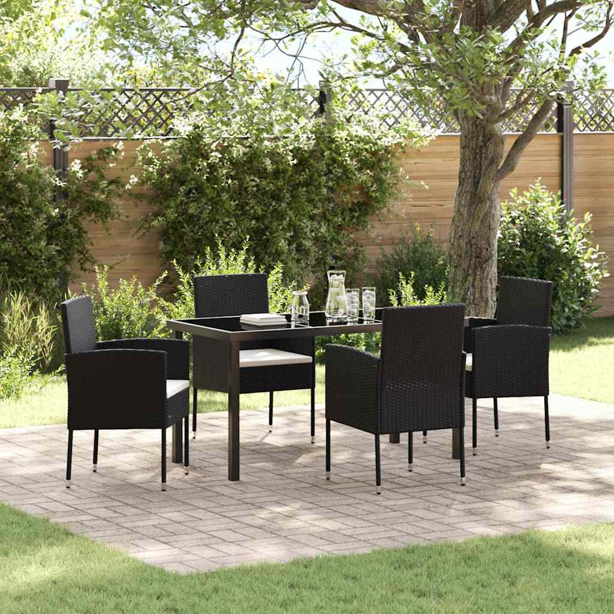Ein Terrassenset mit Tisch und Stühlen steht auf Ziegeln. Grüner Rasen und Bäume befinden sich im Hintergrund mit einem Holzzaun.