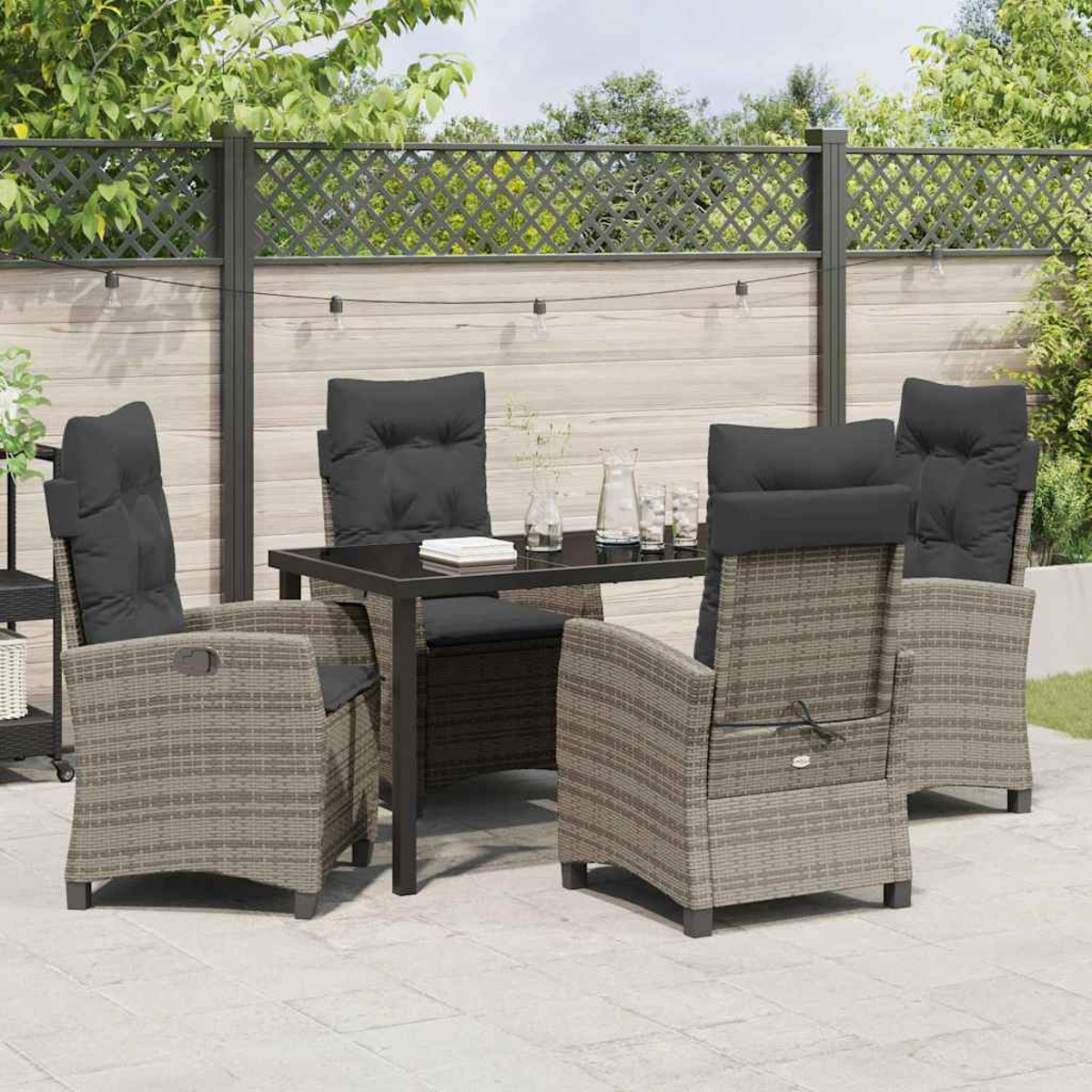 Set da patio esterno con tavolo scuro e sedie con cuscini grigi. Una recinzione e alberi sullo sfondo.