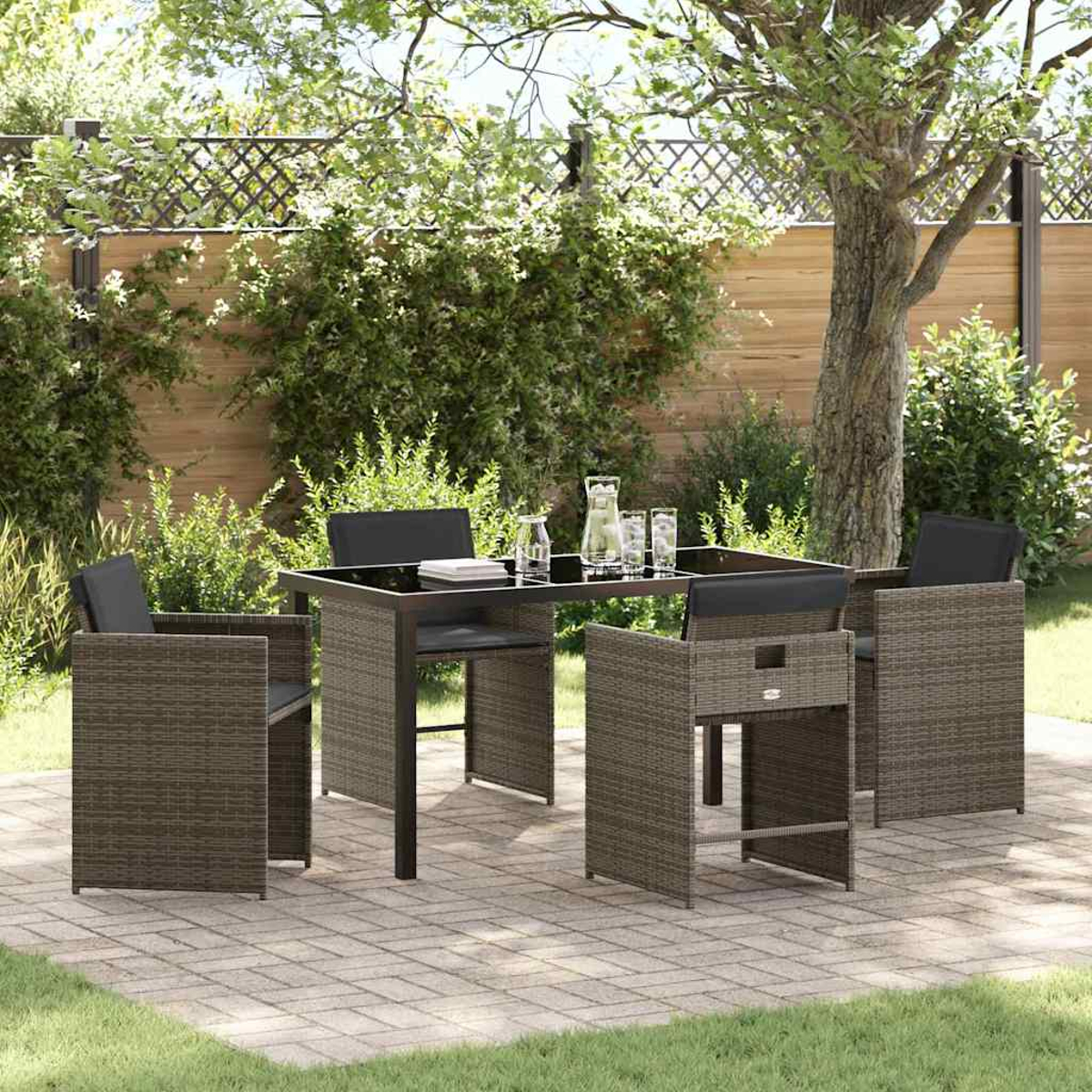Terrassenset im Freien mit Tisch und Stühlen. Der Tisch hat eine schwarze Oberfläche. Die Stühle sind aus Korb mit schwarzen Kissen. Der Hintergrund sind Bäume.