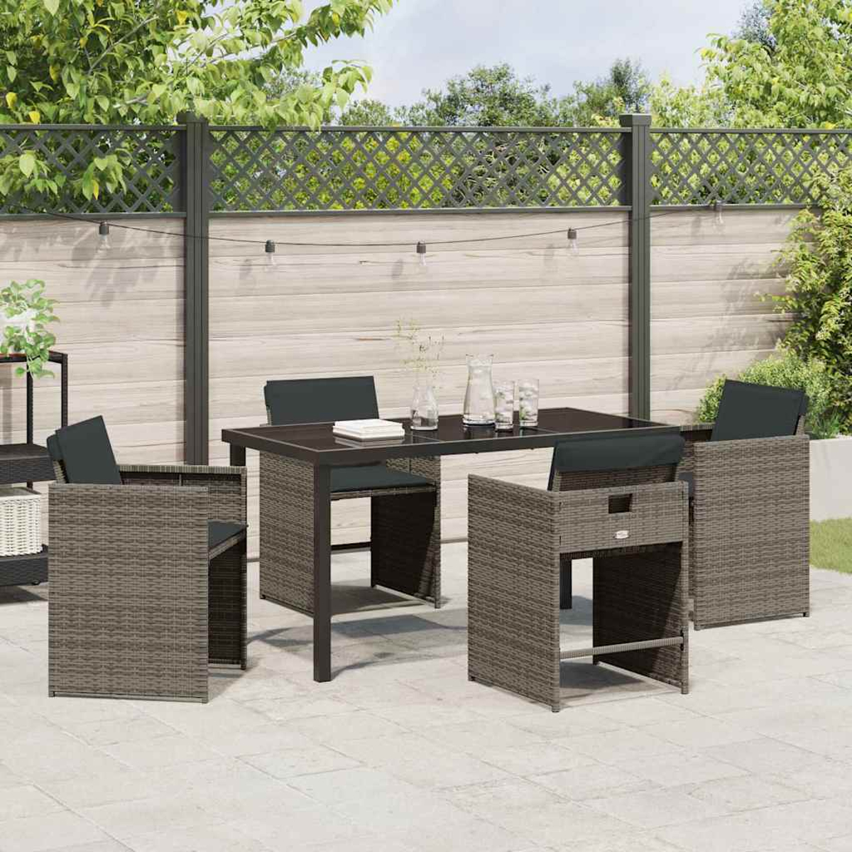 Essgruppe im Freien. Ein dunkler Tisch mit vier Stühlen auf einer Terrasse. Im Hintergrund ein Zaun und Grün.