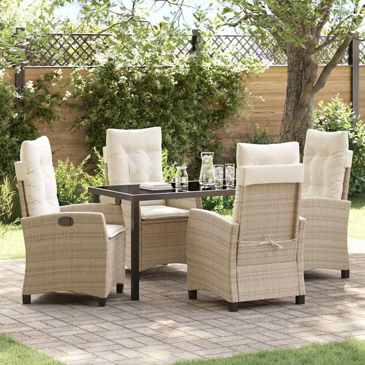 Set da patio esterno con sedie in vimini beige, cuscini color crema, un tavolo con piano in vetro e cristalleria, contro una siepe verde.