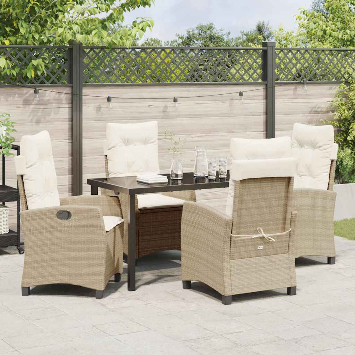 Set da pranzo all'aperto con quattro sedie in vimini, cuscini color crema e un tavolo nero. Su un patio con una recinzione e verde sullo sfondo.