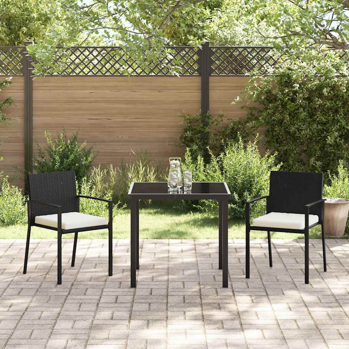 Terrassenmöbel im Freien mit zwei Stühlen, einem Tisch und zwei Gläsern. Im Hintergrund ein Zaun, Pflanzen und ein sonniger Tag.