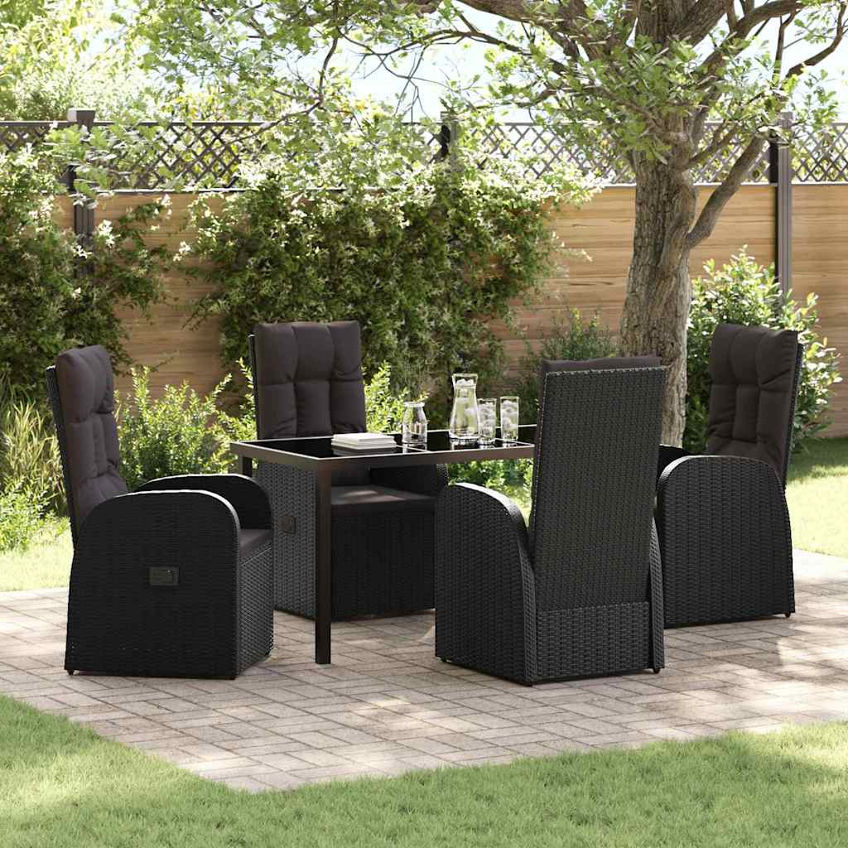 Terrassenset im Freien: schwarze Korbstühle und Tisch. Grünes Gras und Blätter umgeben die Terrasse. Bäume und Zaun im Hintergrund.
