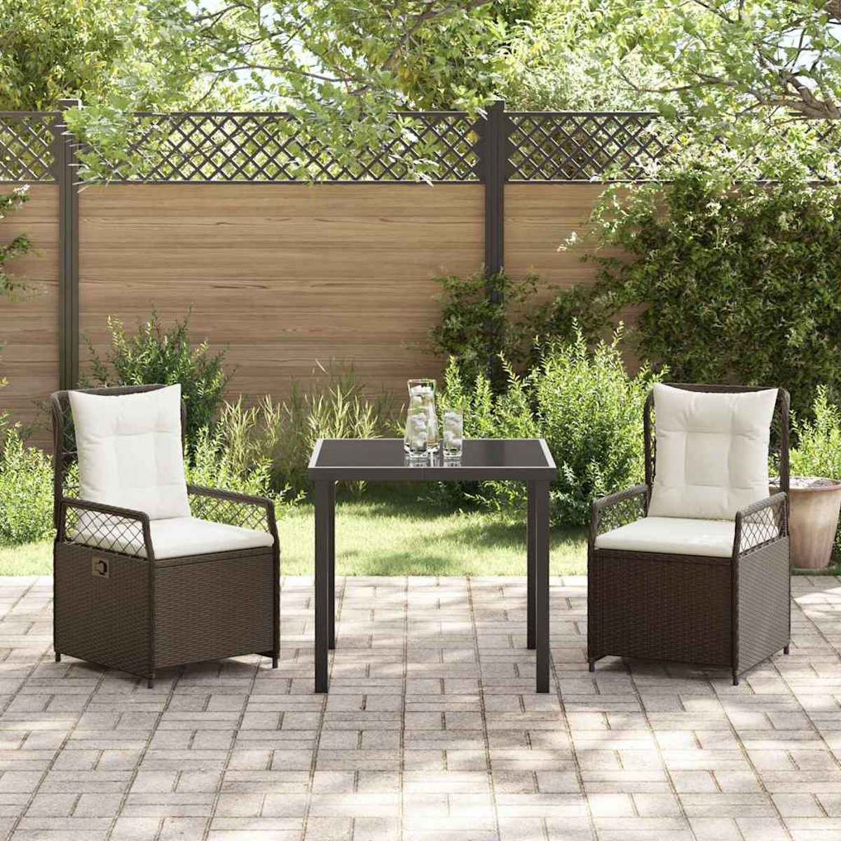Terrassenset im Freien mit zwei Stühlen und einem Tisch. Die Stühle haben weiße Kissen, und auf dem Tisch stehen Gläser. Im Hintergrund sind grüne Pflanzen und ein Zaun zu sehen.
