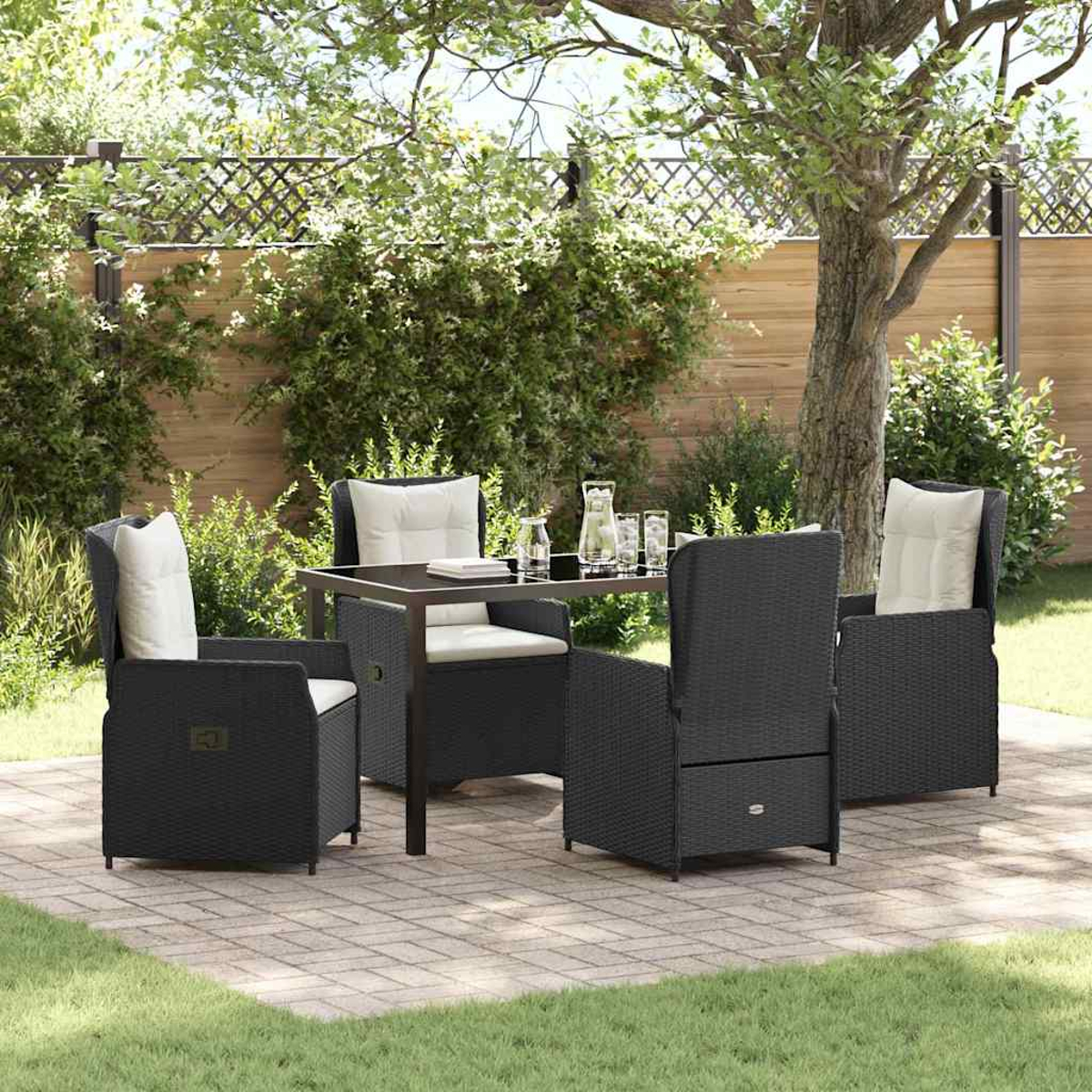Terrassenset: vier schwarze Korbstühle mit weißen Kissen um einen Tisch. Ein Glas Wasser und Pflanzen im Hintergrund.