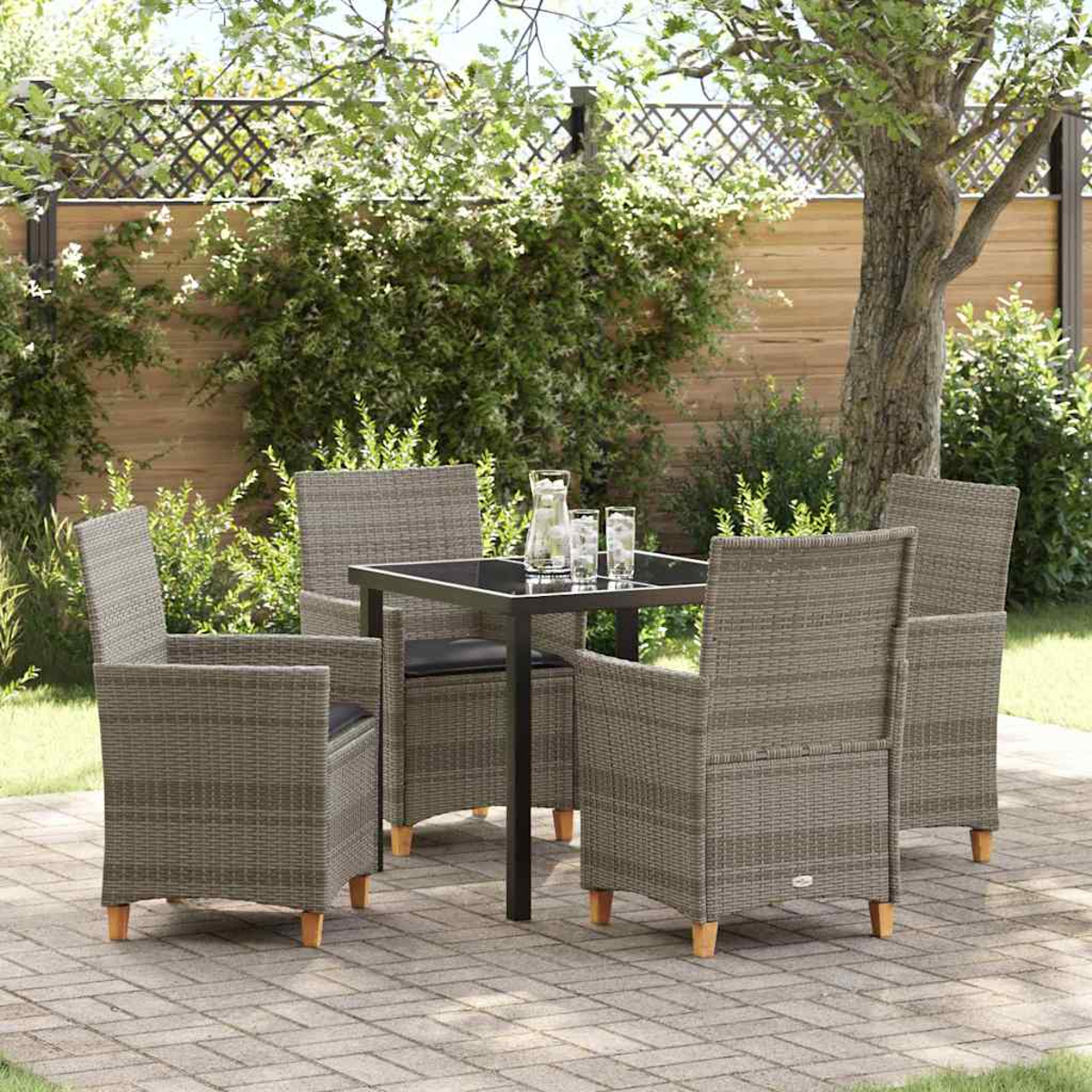 Ein Terrassenset mit Tisch und Stühlen. Auf dem Tisch stehen ein Krug und Gläser. Im Hintergrund sind ein Zaun und Bäume zu sehen.