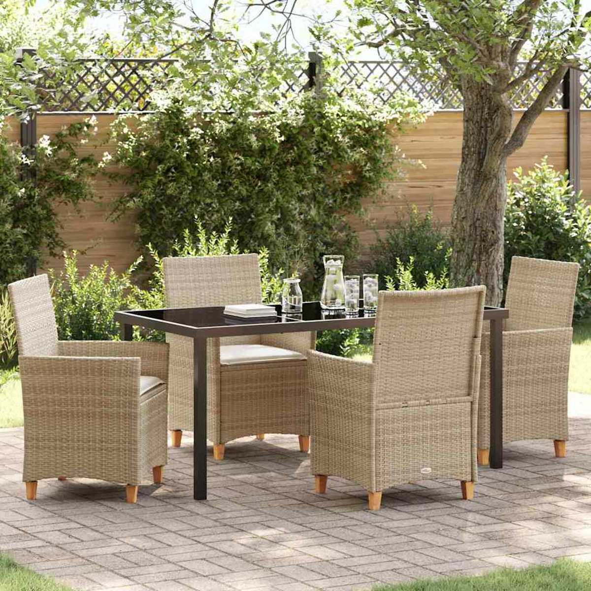 Terrassenset im Freien mit schwarzem Tisch, vier Korbstühlen und Gläsern auf dem Tisch. Grünes Laub und ein Zaun im Hintergrund.