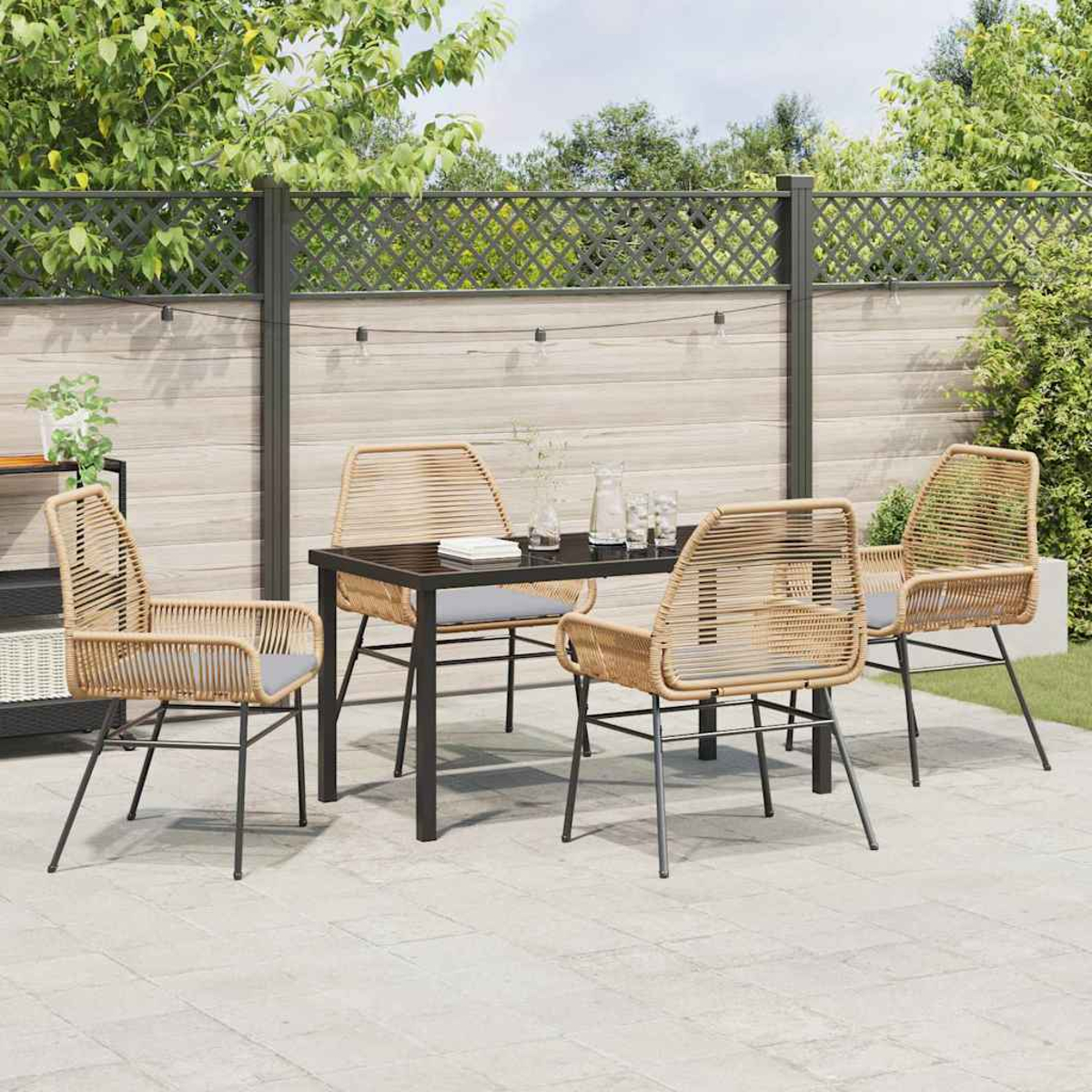 Set da patio esterno con tavolo e quattro sedie. Sedie marrone chiaro con cuscini grigi. Il tavolo è nero. Recinzione in legno e piante sullo sfondo.