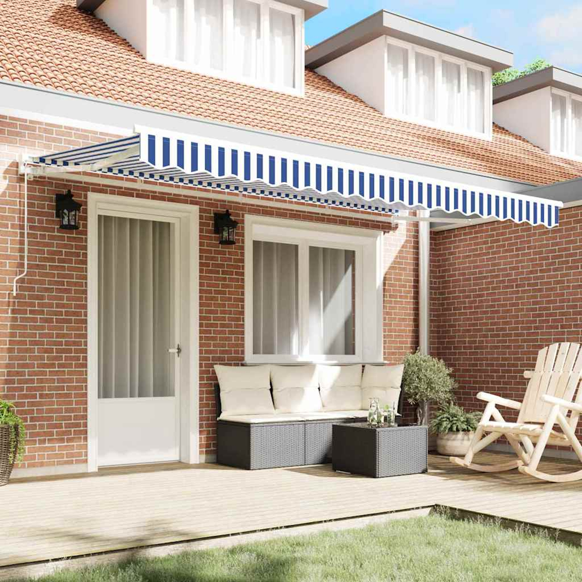 Das Äußere eines Hauses zeigt eine blau-weiß gestreifte Markise. Ein Holzdeck hat Möbel. Rote Backsteinmauer und grünes Gras vorne.