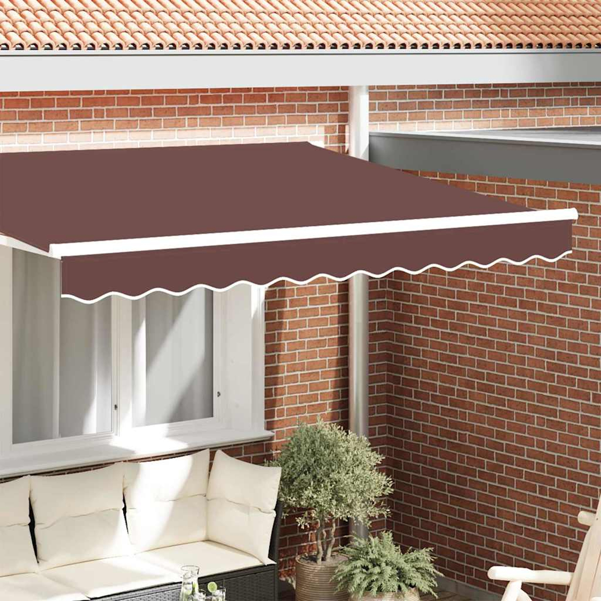 Un toldo marrón con ribete blanco sobre un patio, pared de ladrillo, sofá con cojines blancos y plantas en macetas.