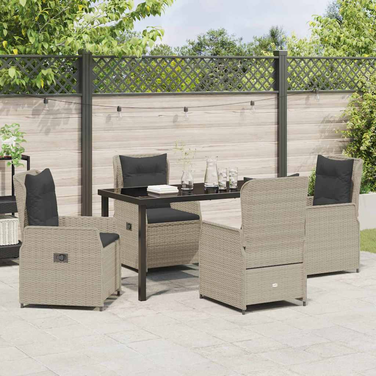 Terrassenset mit Tisch und vier Stühlen. Der Tisch hat eine schwarze Oberfläche. Stühle haben schwarze Kissen. Hintergrundzaun und Pflanzen.