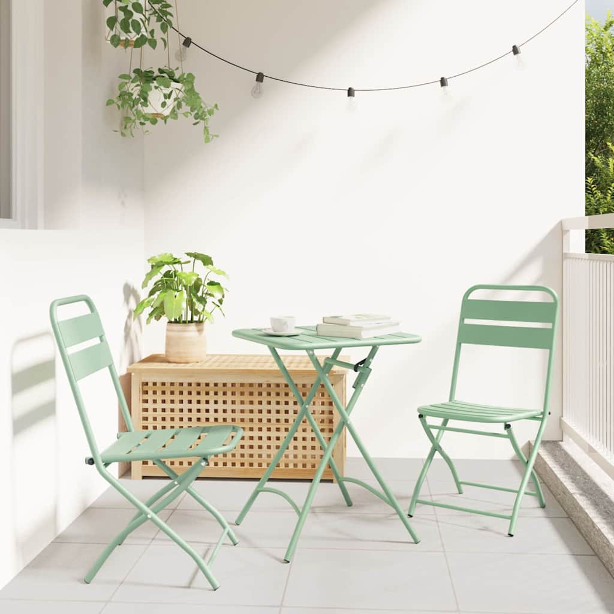 Ein kleines Terrassenset mit zwei Stühlen und einem Tisch in Hellgrün. Ein Holzschrank mit Pflanze und Lichterketten.
