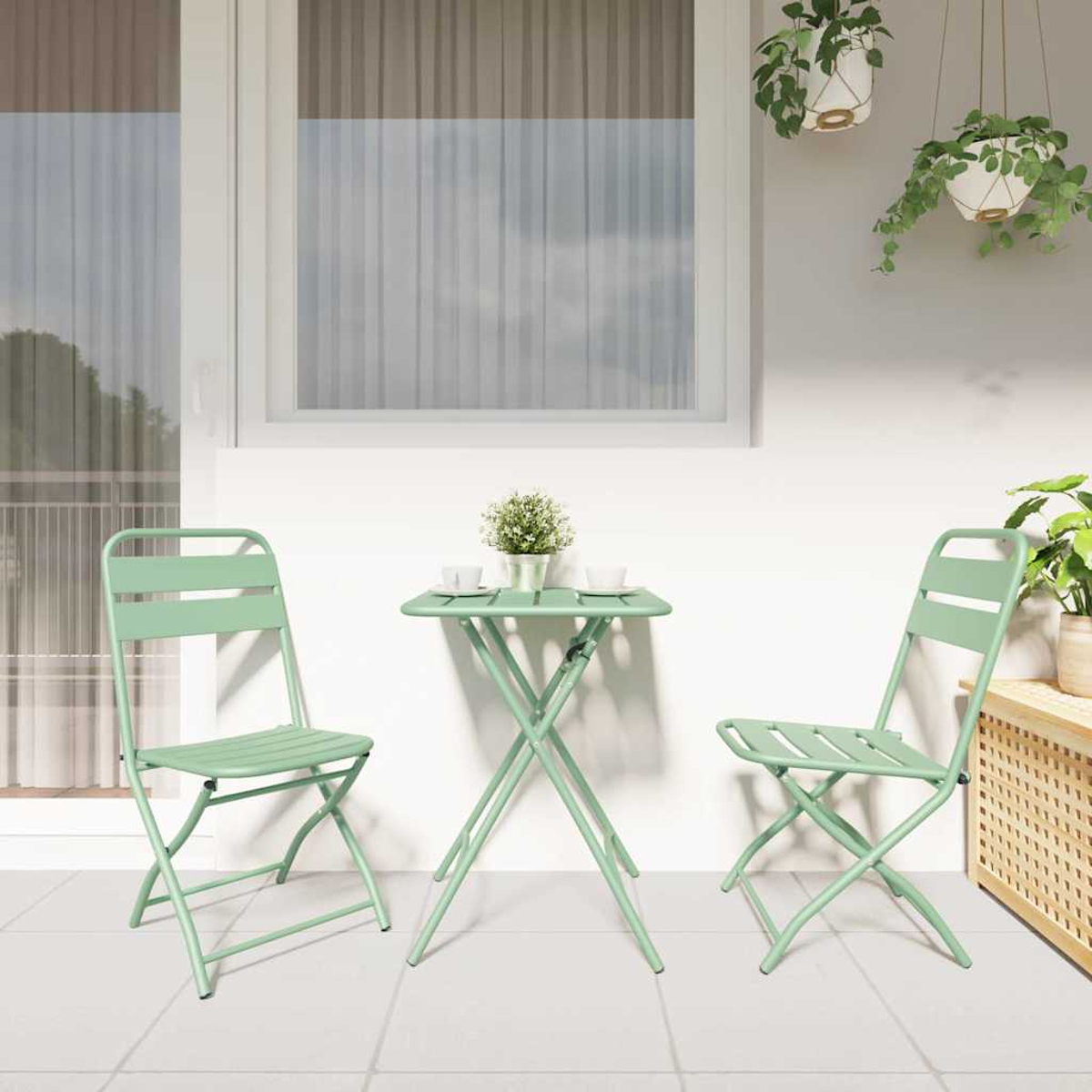 Ein Terrassenset mit zwei grünen Stühlen und einem Tisch. Weiße Wand mit Fenster, zwei Hängetöpfen und anderen Pflanzen.