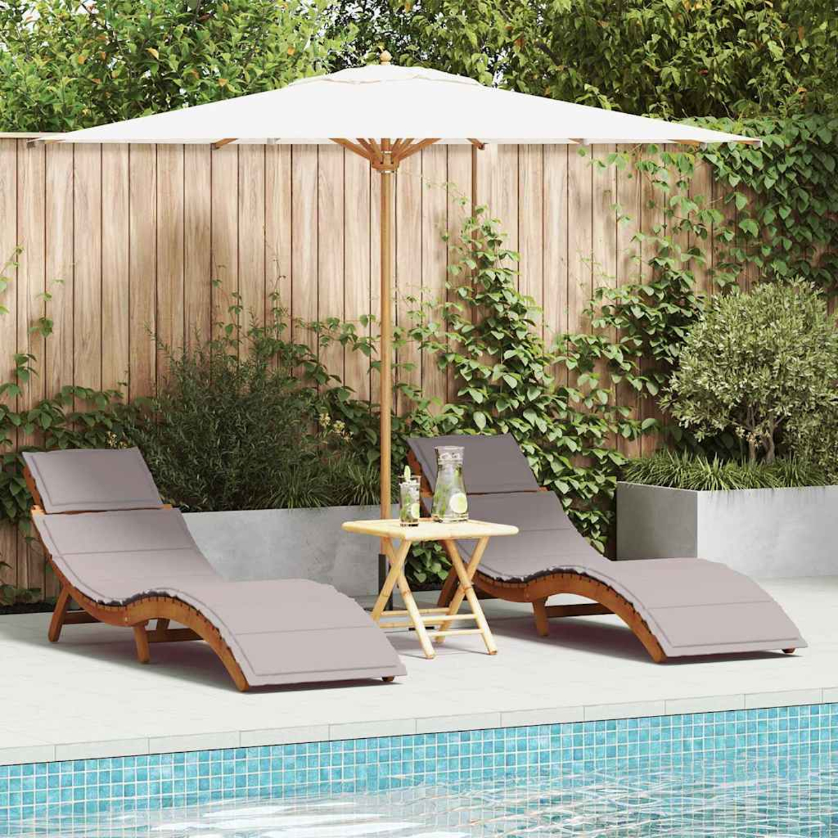 Zwei graue Liegestühle am Pool mit weißem Sonnenschirm und kleinem Tisch. Hintergrund: Holzzaun und Grün.