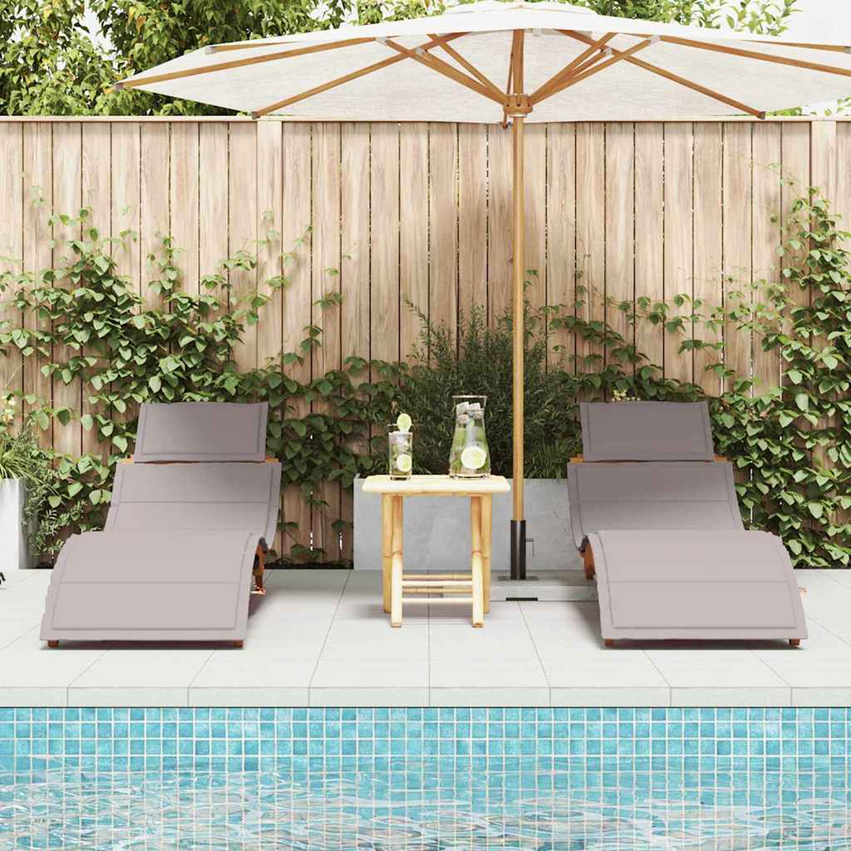 Zwei graue Liegestühle an einem Pool mit einem kleinen Tisch und Sonnenschirm. Im Hintergrund befinden sich ein Holzzaun und Kletterpflanzen.