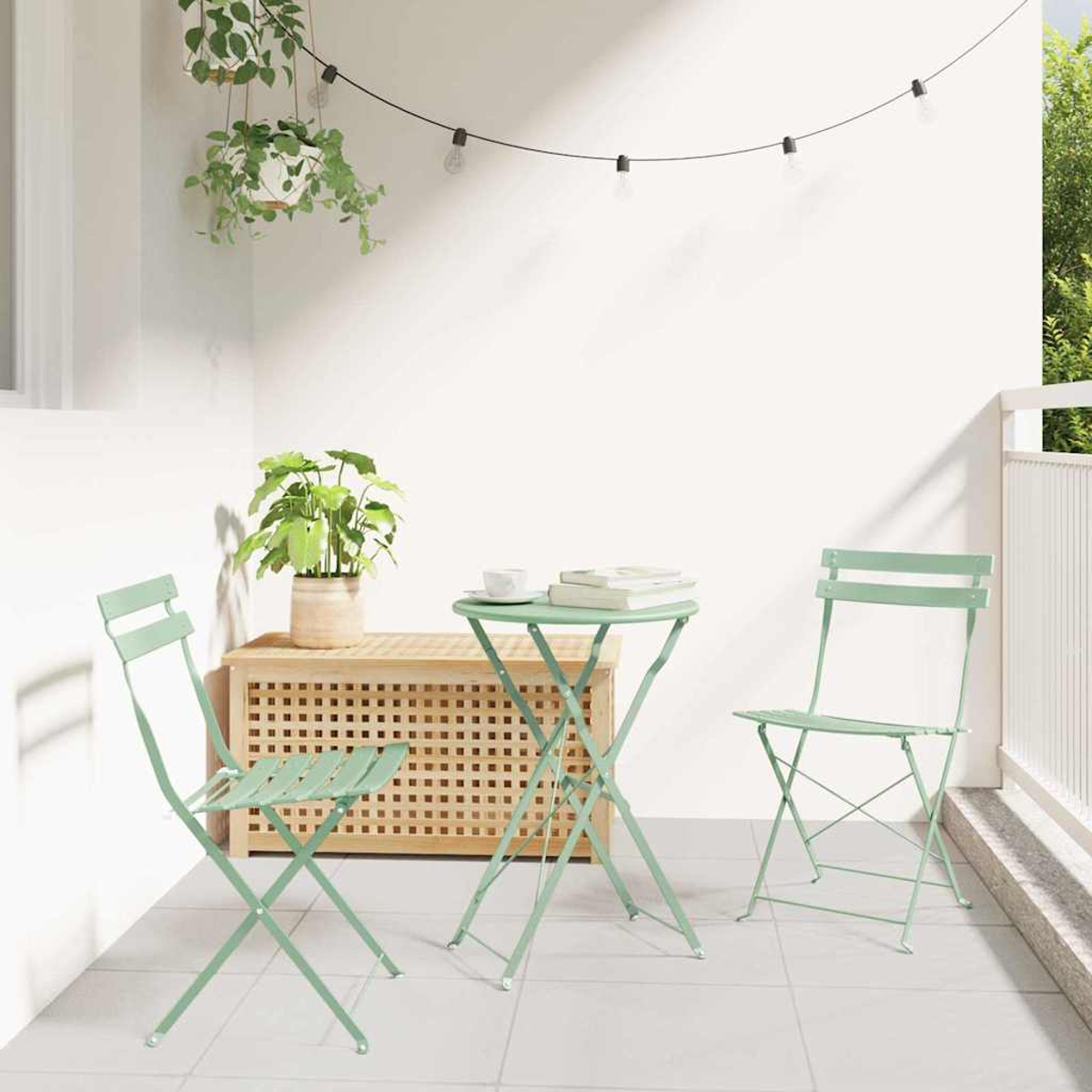 Ein kleiner Balkon mit grünen Stühlen und einem Tisch. Eine Pflanze steht auf dem Tisch und in einem Topf. Hängelampen oben.