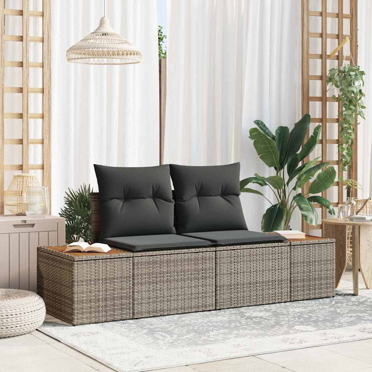 Outdoor-Rattansofa mit grauen Kissen. Weiße Vorhänge, Pflanzen und eine gewebte Lampe im Hintergrund. Ein Buch liegt auf dem Sofa.