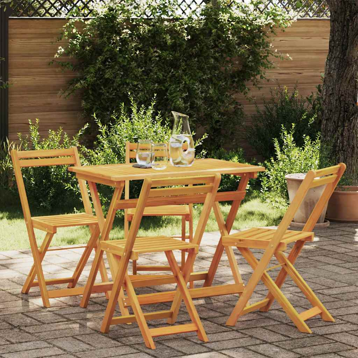 Holz-Gartentisch-Set mit vier Stühlen. Ein Krug und Gläser auf dem Tisch. Grüne Pflanzen und Bäume im Hintergrund.