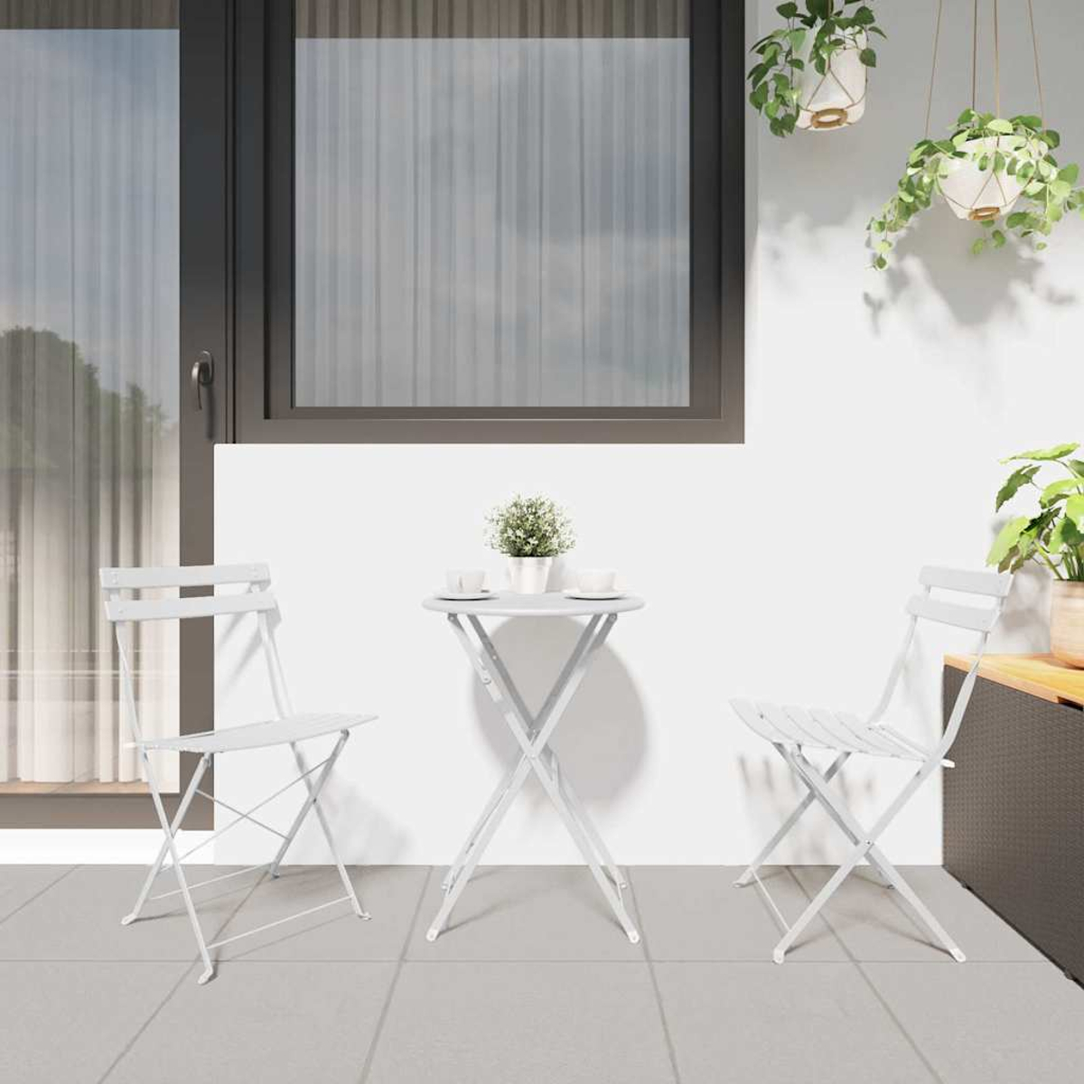 Ein weißes Terrassenset mit zwei Stühlen und einem kleinen Tisch. Pflanzen hängen von der Decke und stehen auf einem Regal.