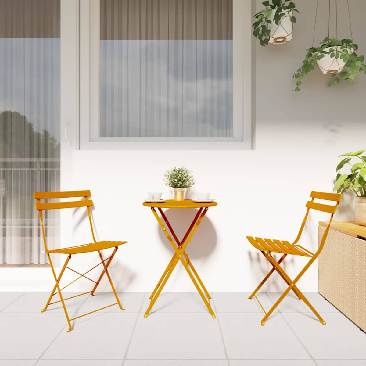 Ein gelbes Bistrotisch-Set auf einer Terrasse mit einem kleinen runden Tisch, zwei Stühlen und Pflanzen. Fenster und Hängepflanzen im Hintergrund.