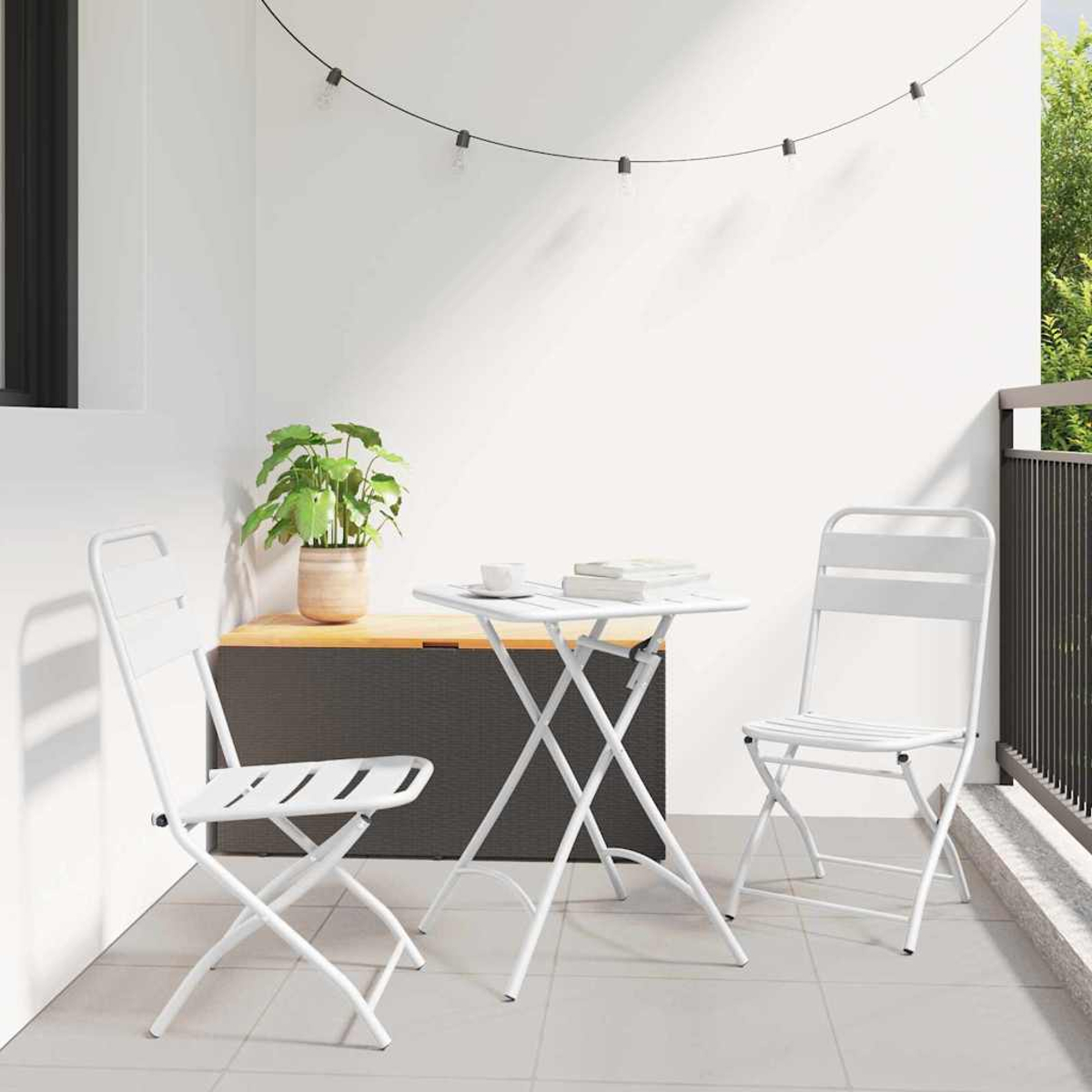 Ein Balkon mit weißem Tisch und Stühlen. Ein Blumentopf steht auf einer Holzkiste. Lichterketten hängen darüber.