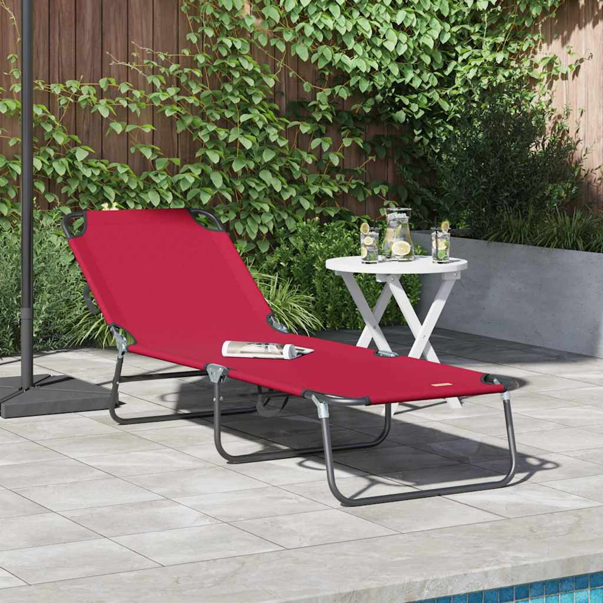 Eine rote Sonnenliege steht auf einer Terrasse, daneben ein weißer Tisch mit Getränken und im Hintergrund ein Holzzaun.