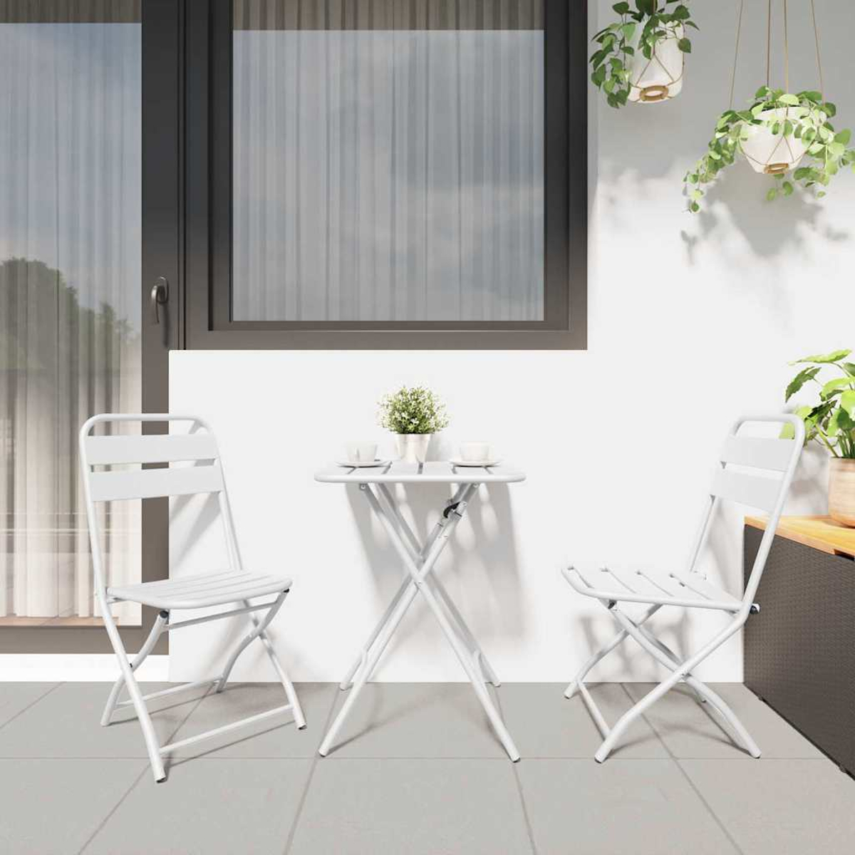 Ein weißer Tisch und zwei Stühle auf einer Terrasse. Eine kleine Pflanze steht auf dem Tisch. Hängepflanzen und ein Fenster sind im Hintergrund.