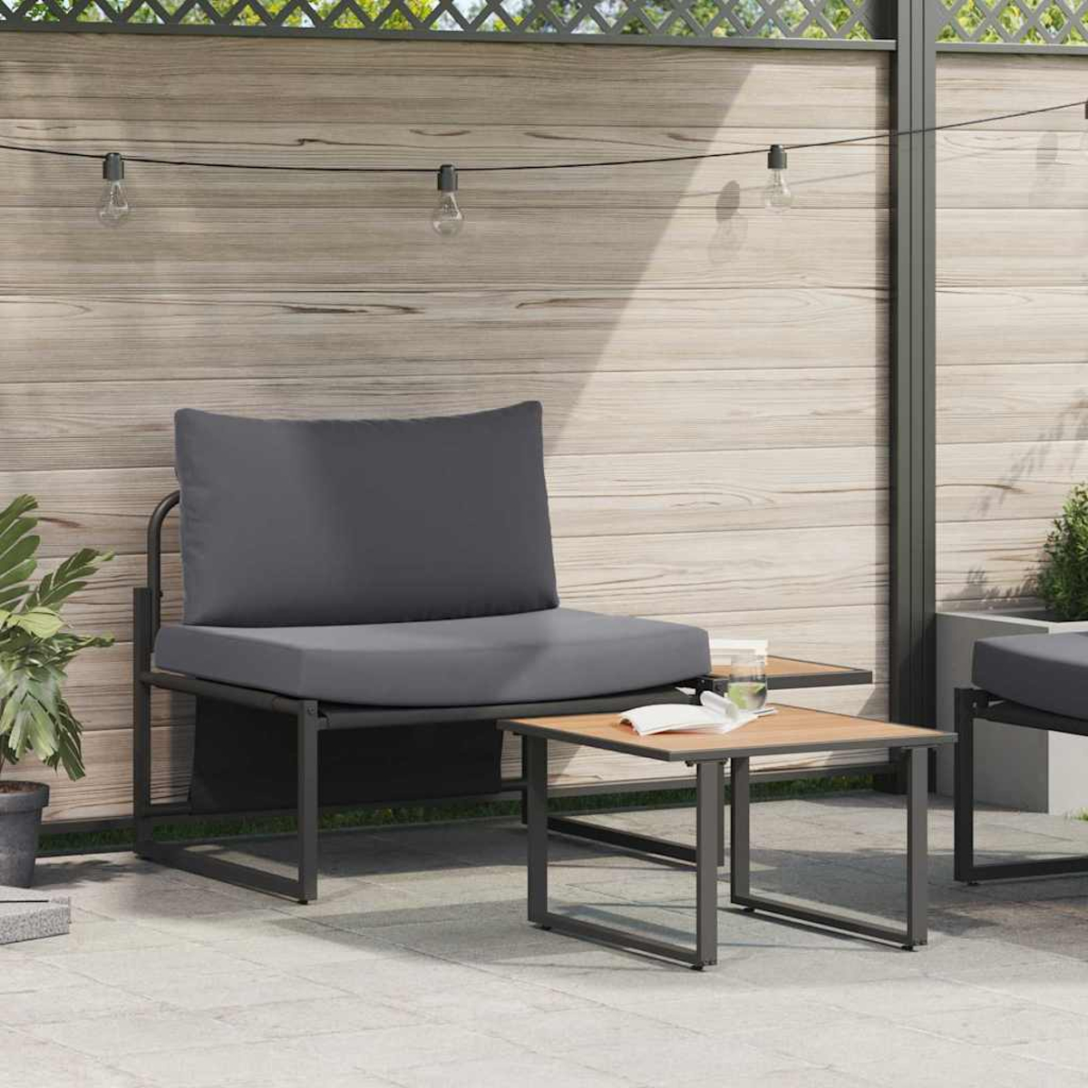 Asientos al aire libre con cojín gris, mesita de madera con libro y vaso, y valla de madera de fondo.