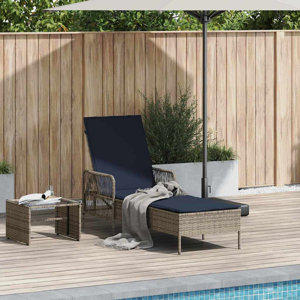 Eine Terrassenszene mit Liegestuhl, Beistelltisch und Sonnenschirm in der Nähe eines Pools. Eine Decke liegt auf dem Stuhl. Holzzaun im Hintergrund.