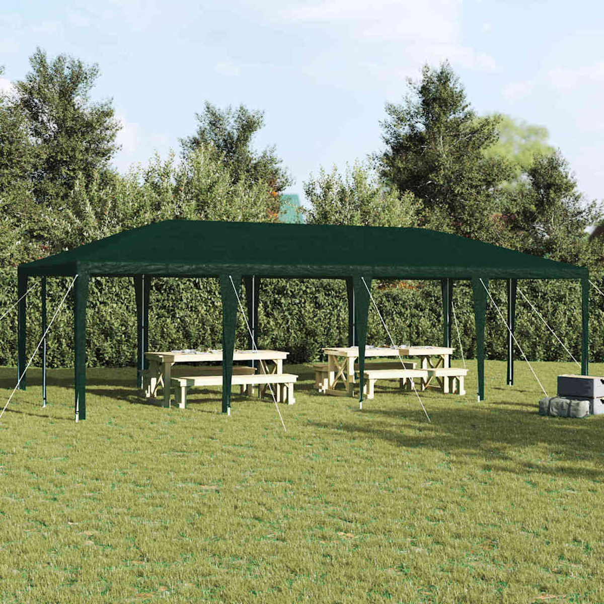 Una tettoia verde sopra tavoli da picnic sull'erba. Alberi e cespugli sullo sfondo sotto un cielo blu.