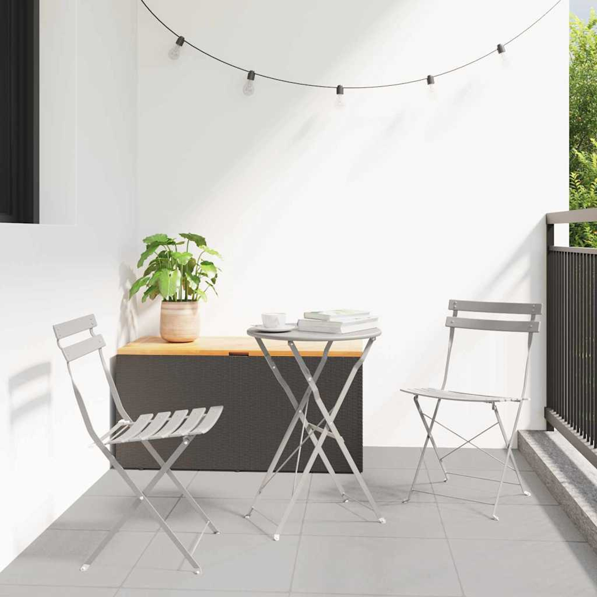 Kleine Außenterrasse mit Tisch, zwei Stühlen, einer Pflanze und Lichterketten. Der Boden ist gefliest und die Wand ist weiß.