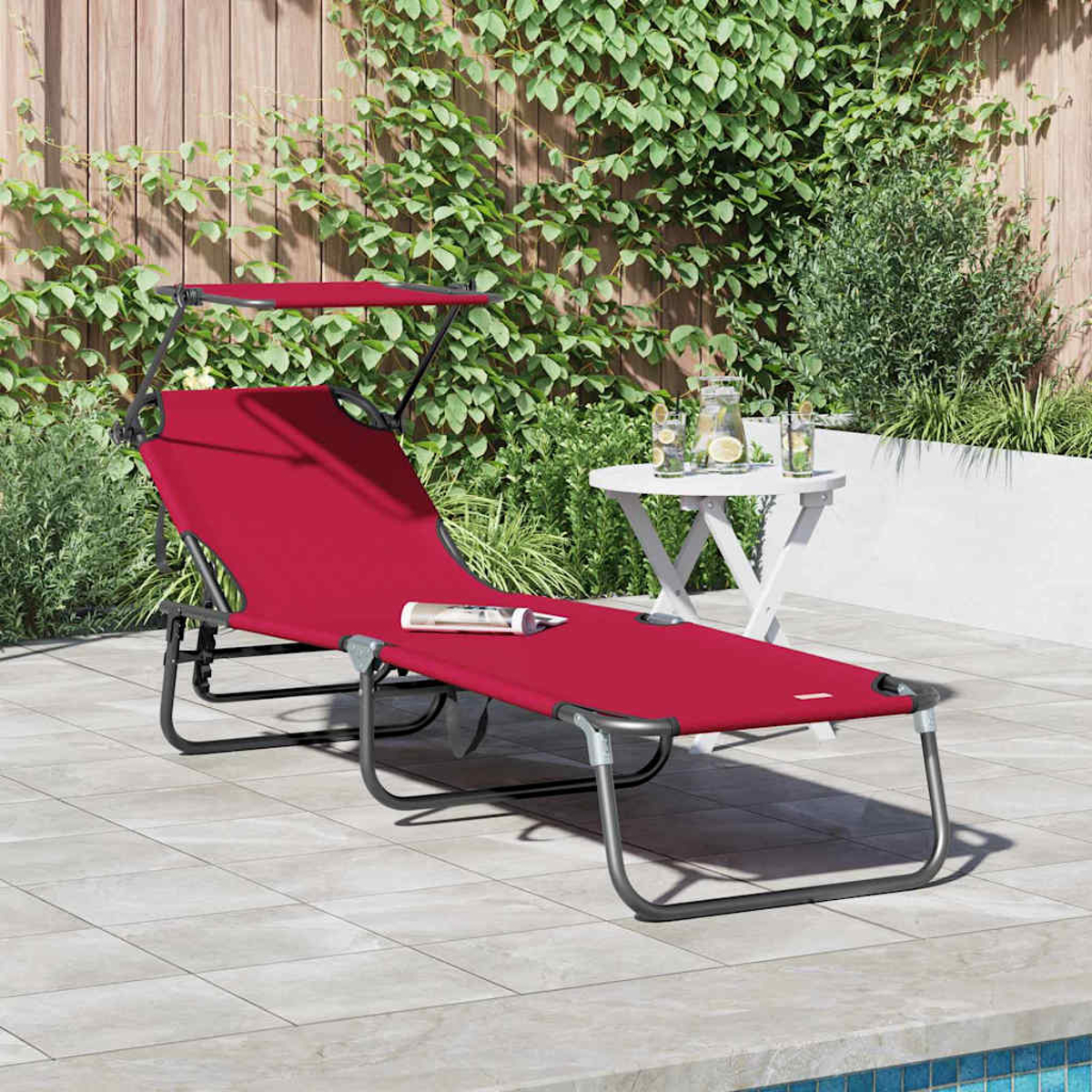 Eine rote Sonnenliege mit Baldachin steht auf einer Terrasse. Im Hintergrund steht ein kleiner weißer Tisch mit Getränken in der Nähe von Grün.