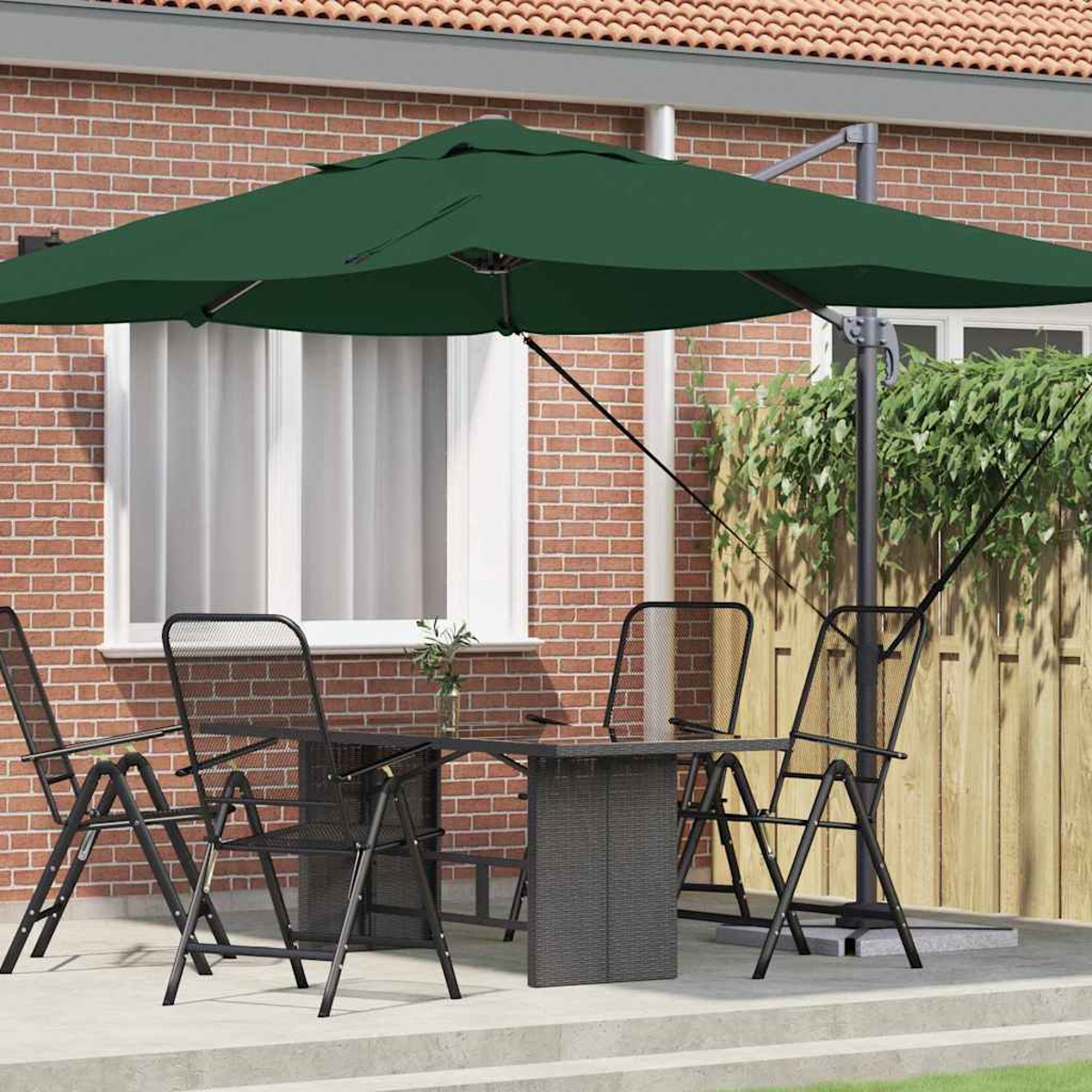 Scena del patio con ombrellone verde scuro, tavolo e sedie neri. Muro di mattoni sullo sfondo, recinzione in legno con vegetazione.