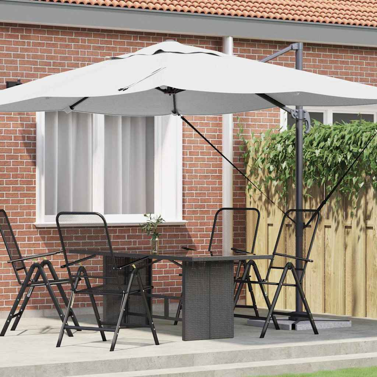 Set da patio all'aperto: tavolo, sedie e un grande ombrello bianco. Muro di mattoni e recinzione in legno sullo sfondo.
