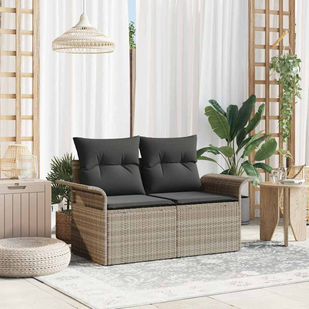 Ein Rattansofa mit grauen Kissen steht auf einem Teppich. Pflanzen, ein Beistelltisch und eine Hängeleuchte sind ebenfalls vorhanden.