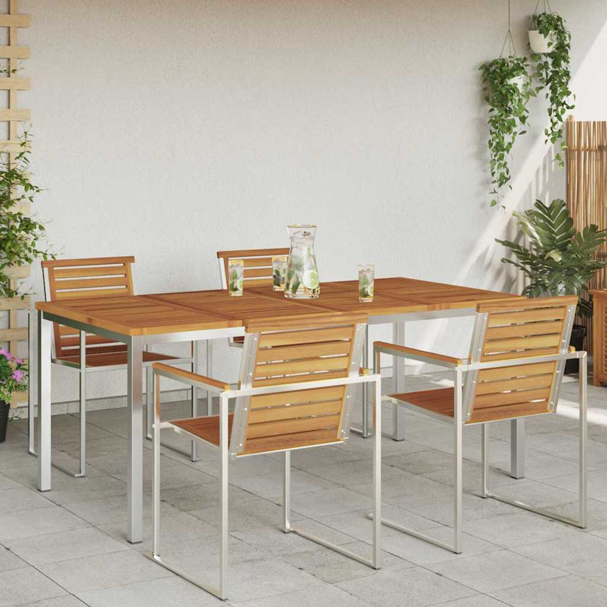 Essgruppe im Freien mit Holztisch und Stühlen. Ein Krug und Gläser mit Eis stehen auf dem Tisch. Pflanzen schmücken den Hintergrund.