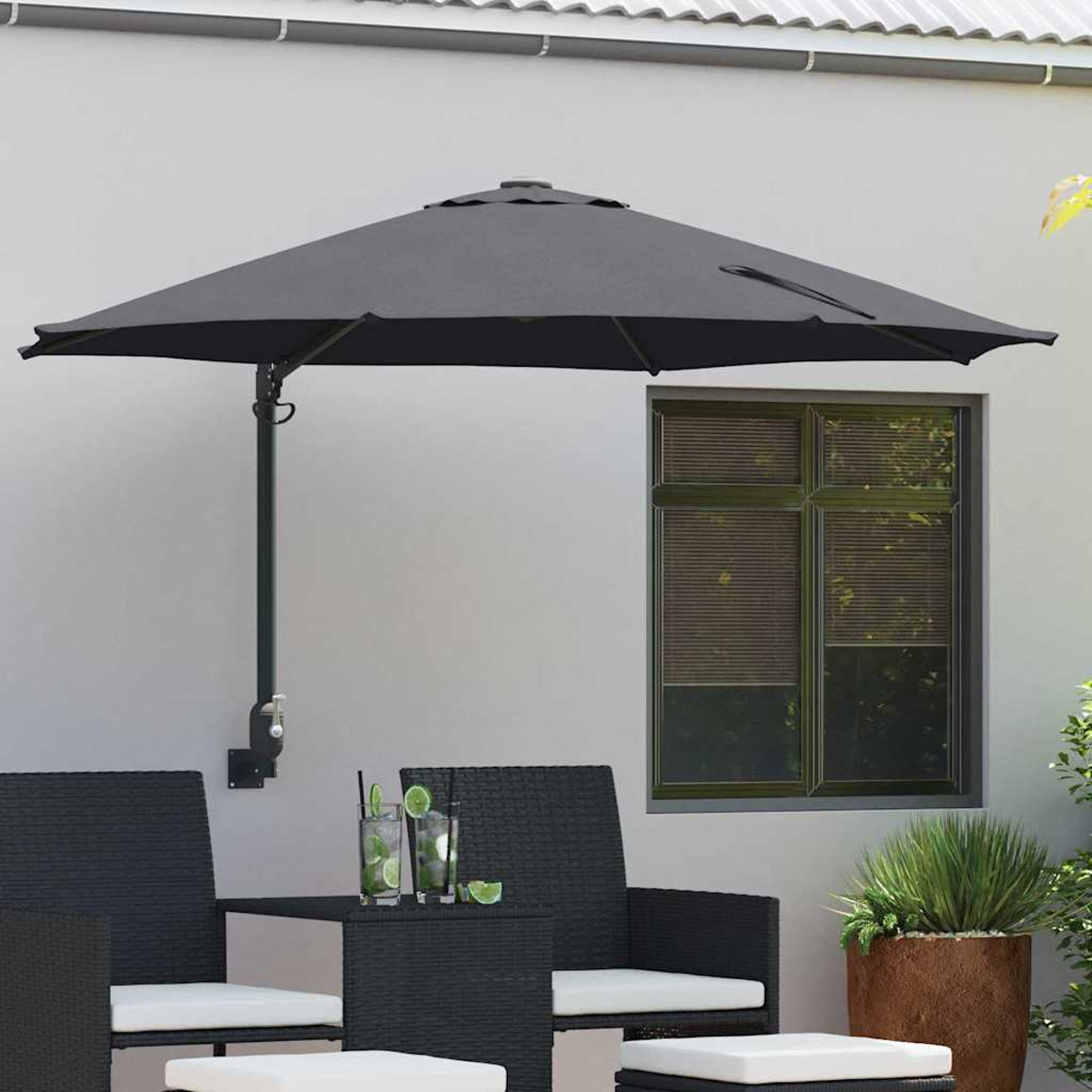 Una scena del patio con un ombrello grigio attaccato al muro, mobili neri, bevande e una finestra con persiane. Una pianta in vaso è visibile.