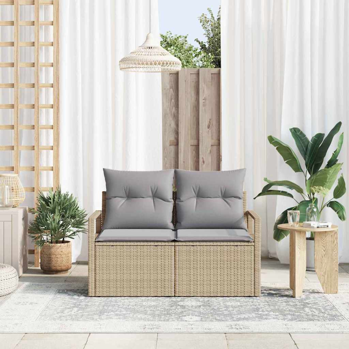 Escena al aire libre con un sofá de ratán con cojines grises, una mesa pequeña y plantas. Cortinas blancas y una valla de madera al fondo.