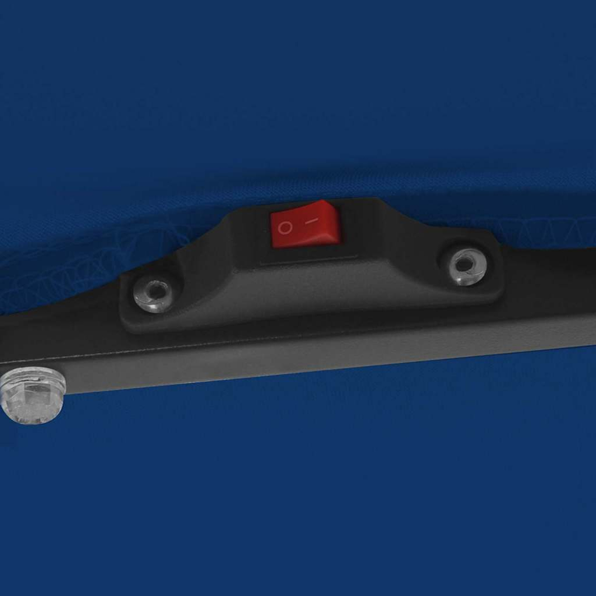Primo piano di un componente in plastica nera con un interruttore rosso di accensione/spegnimento. Un tessuto blu forma lo sfondo, un piedino di plastica trasparente è visibile.