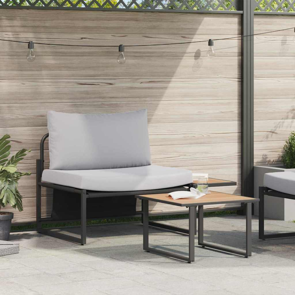 Gartenmöbel mit grauem Kissen, kleiner Tisch mit Buch, Lichterkette und Holzzaun im Hintergrund.