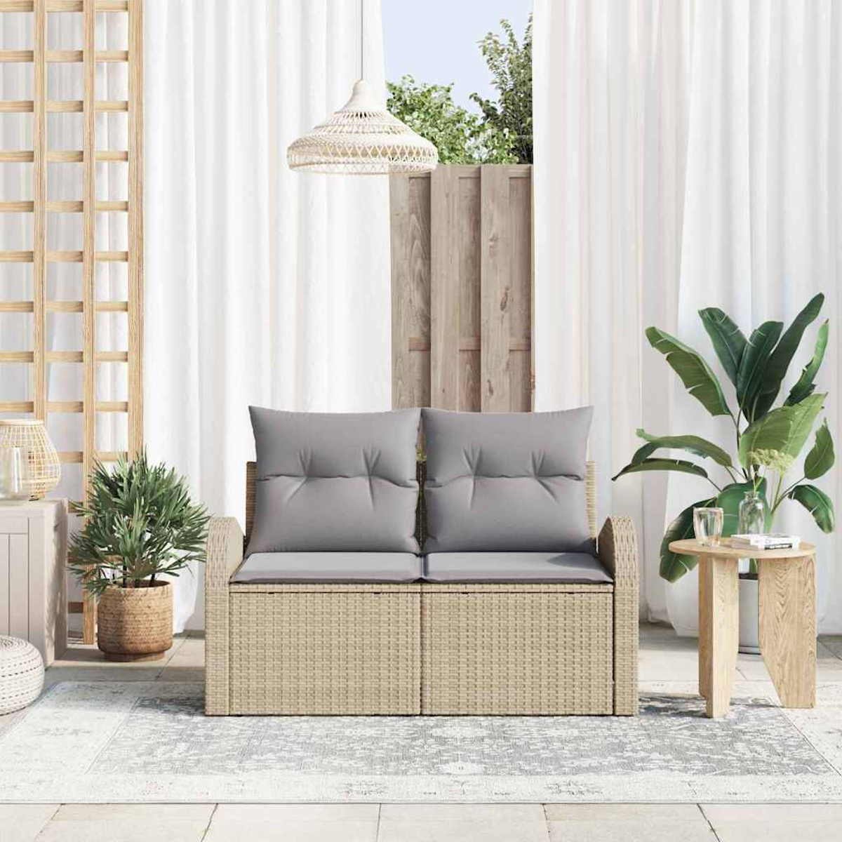 Eine Terrassenszene mit einer beigen Korbliege mit grauen Kissen, einem kleinen Holztisch und großen grünen Pflanzen.