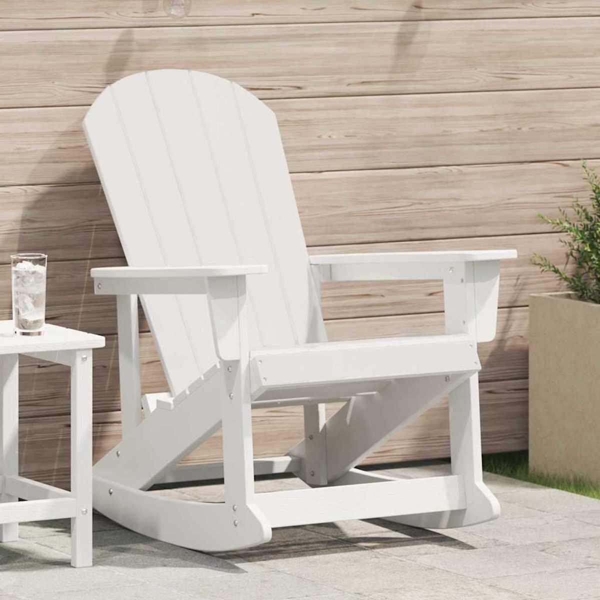 Ein weißer Adirondack-Stuhl auf einer Terrasse. Ein Beistelltisch mit einem Glas Wasser. Holz Hintergrund. Eine Topfpflanze ist rechts.