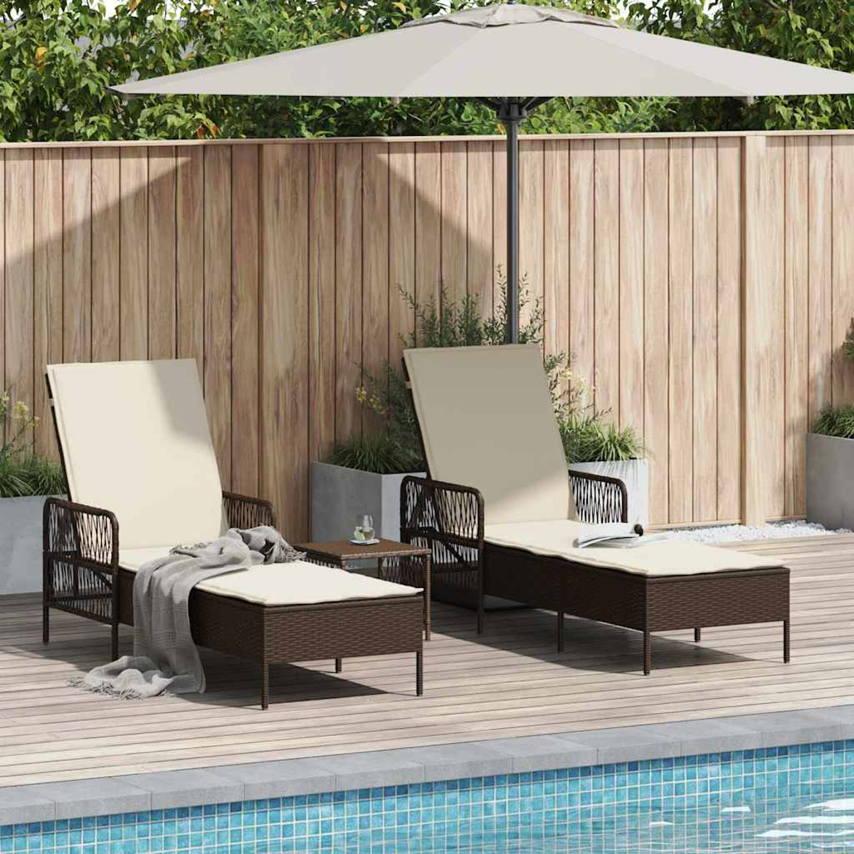 Zwei braune Korbliegen mit cremefarbenen Kissen unter einem beigen Sonnenschirm an einem Pool. Holzzaun und Pflanzen im Hintergrund.